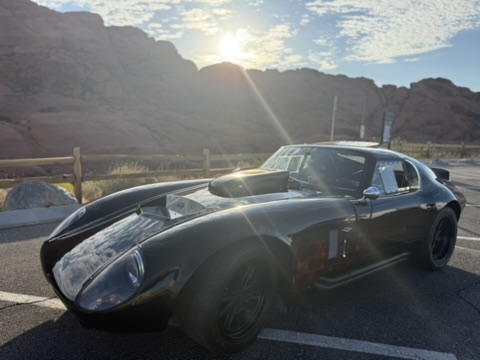 Factory Five Daytona replica in front of red rocks with sun flare